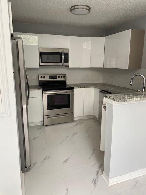 A modern kitchen features white cabinets, stainless steel appliances, and white marble-patterned tile flooring — 575 BLOOMINGTON COURT UNIT 20, ALTAMONTE SPRINGS, FL