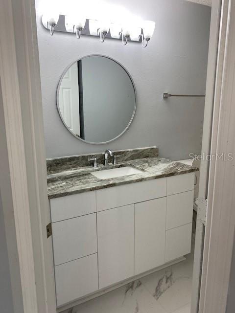 A bathroom features a white vanity with a marble countertop, a round mirror, and light fixtures — 575 BLOOMINGTON COURT UNIT 20, ALTAMONTE SPRINGS, FL