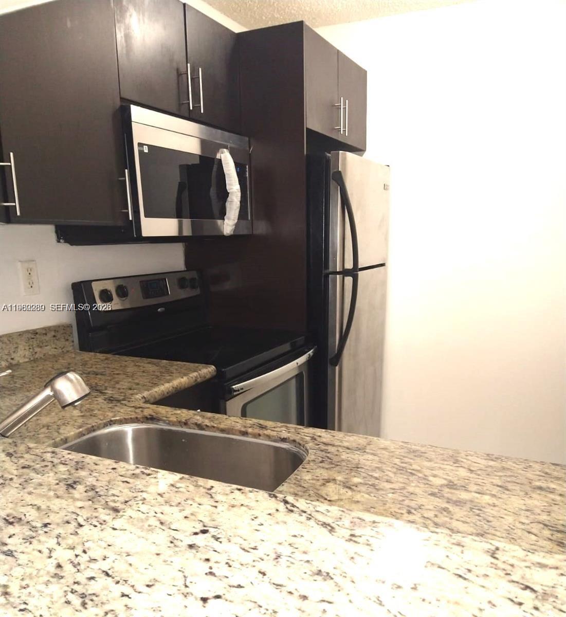 A kitchen features dark wood cabinets, stainless steel appliances, and speckled granite countertops — 488 NW 165 St Rd # 310, Miami FL 33169, MIAMI, FL