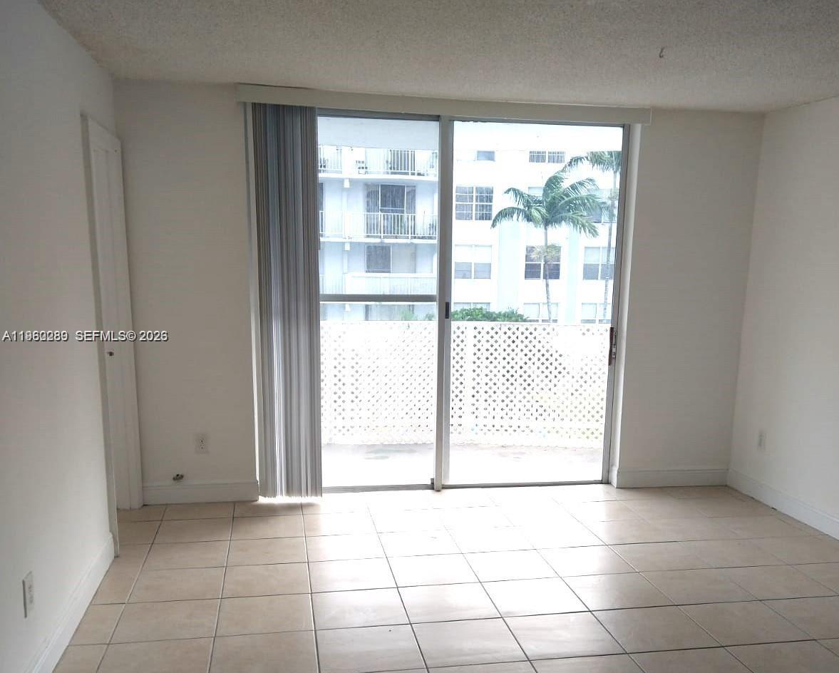 An empty room features light-colored tile flooring, white walls, and a sliding glass balcony door — 488 NW 165 St Rd # 310, Miami FL 33169, MIAMI, FL