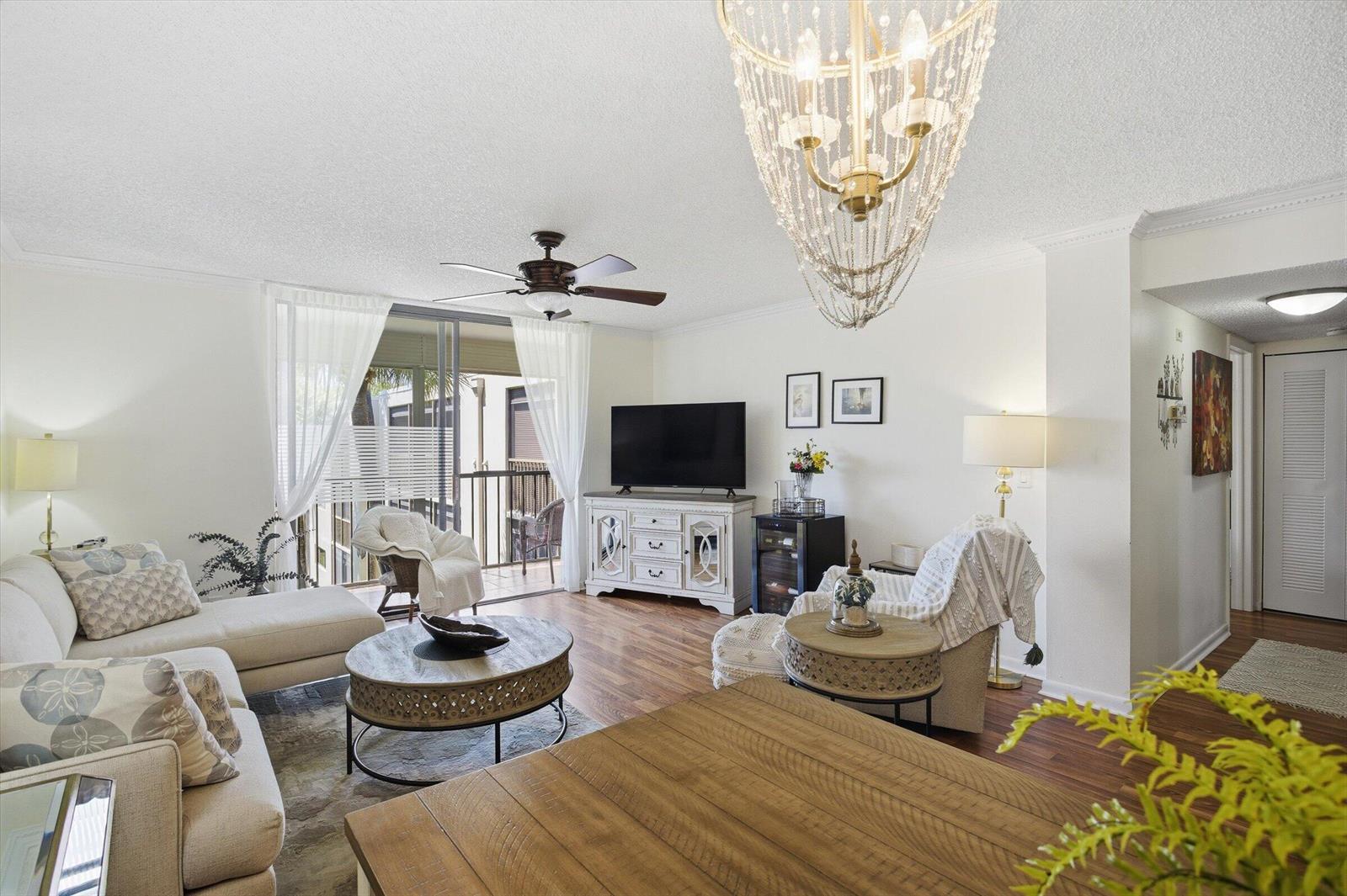 A bright living room features a crystal chandelier, wood-look flooring, and a sliding glass door — 5370 Las Verdes Circle # 303, Delray Beach FL 33484, DELRAY BEACH, FL