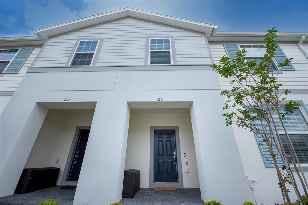 The exterior of a two-story townhouse features white stucco, light gray siding, and two dark blue doors — 126 JETTY WAY, DAVENPORT, FL