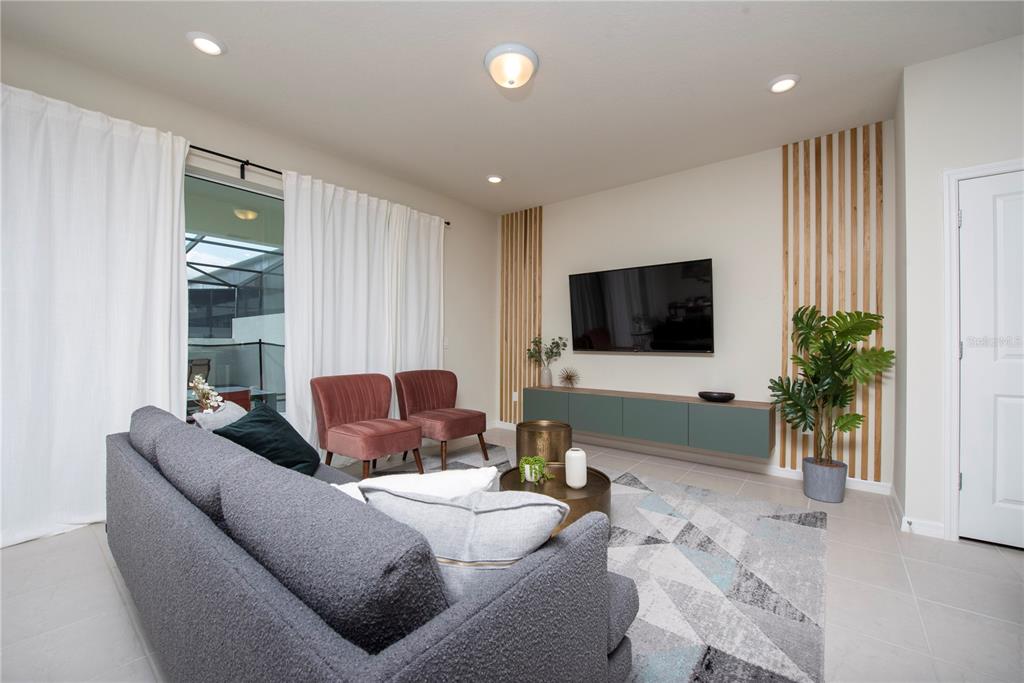 A living room features a grey sofa, two pink chairs, a wall-mounted television, and wood-slat accents — 126 JETTY WAY, DAVENPORT, FL