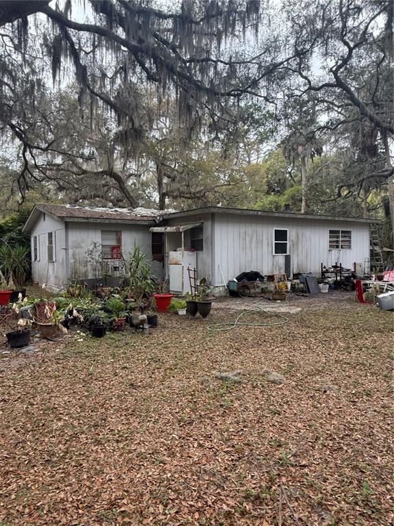 An exterior view of a weathered, single-story house with light-colored siding and surrounding potted plants — 1730 S PALM AVENUE, HOMOSASSA, FL