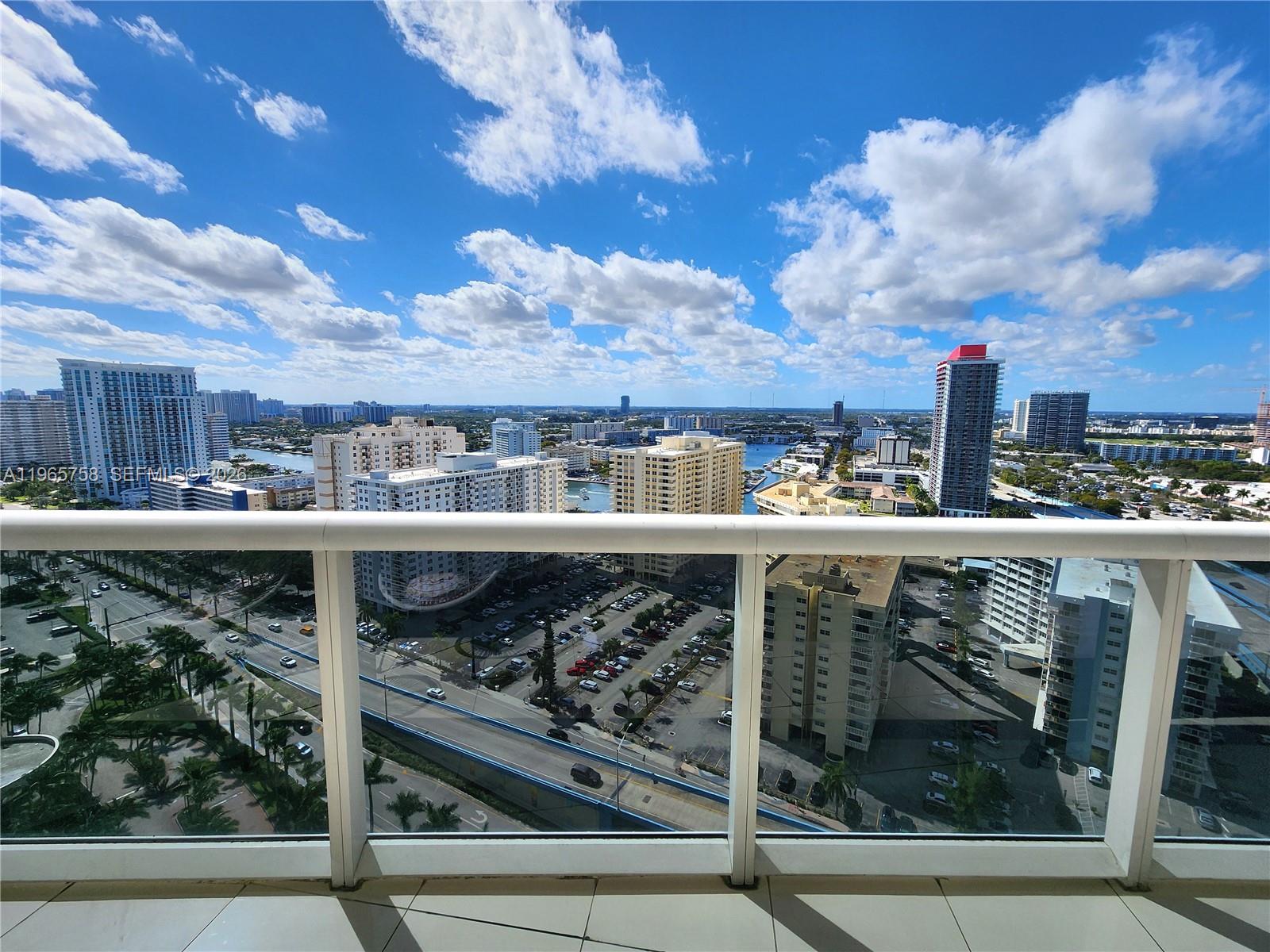 A high-rise balcony overlooks a city skyline, a parking lot, and a waterway — 1800 S Ocean Dr # 2406, Hallandale Beach FL 33009, HALLANDALE BEACH, FL