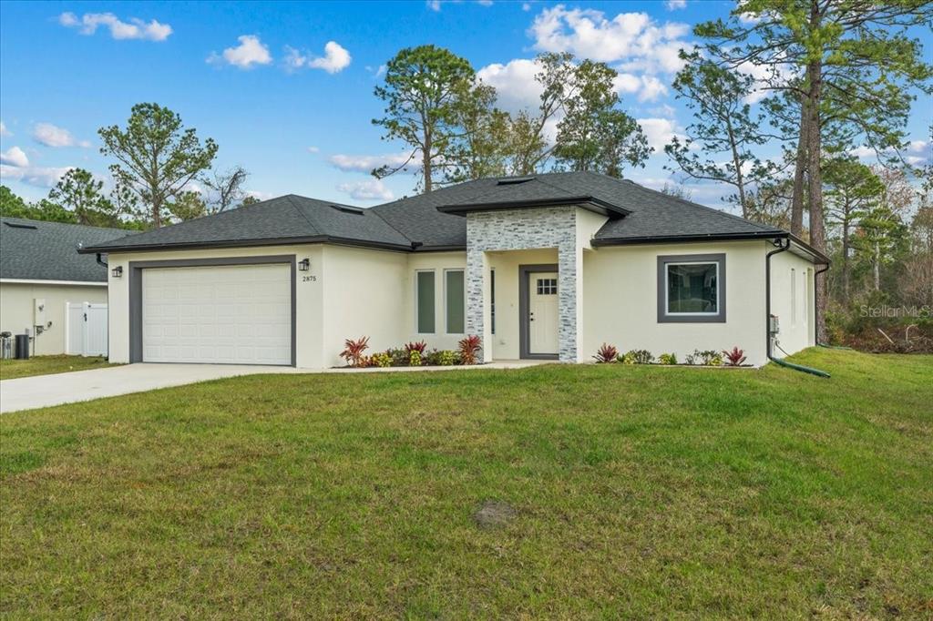 A single-story house with a white stucco exterior, a two-car garage, and stone entryway accents — 2875 E SLATER DRIVE, DELTONA, FL
