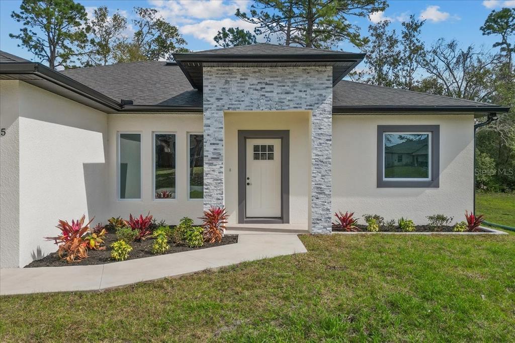 The exterior of a modern house features a stone-accented entryway and a white stucco facade — 2875 E SLATER DRIVE, DELTONA, FL