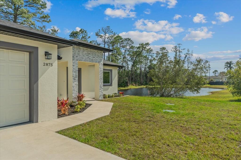 A modern house exterior features a stone-accented facade, a concrete walkway, and a pond view — 2875 E SLATER DRIVE, DELTONA, FL