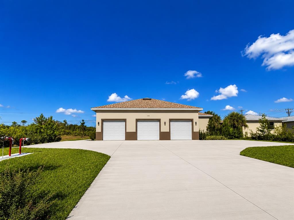 A detached three-car garage with a concrete driveway sits under a bright blue sky — 289 BOUNDARY BOULEVARD UNIT 204, ROTONDA WEST, FL