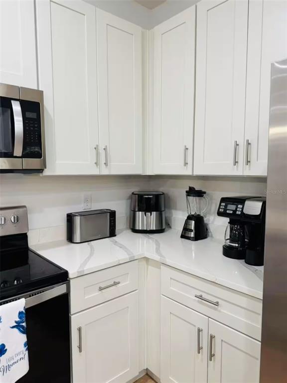 A kitchen corner features white cabinets, a quartz countertop, and various stainless steel appliances — 289 BOUNDARY BOULEVARD UNIT 204, ROTONDA WEST, FL