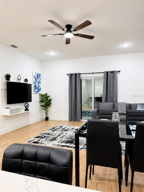 This living and dining area features a ceiling fan, a wall-mounted television, and wood-look flooring — 289 BOUNDARY BOULEVARD UNIT 204, ROTONDA WEST, FL