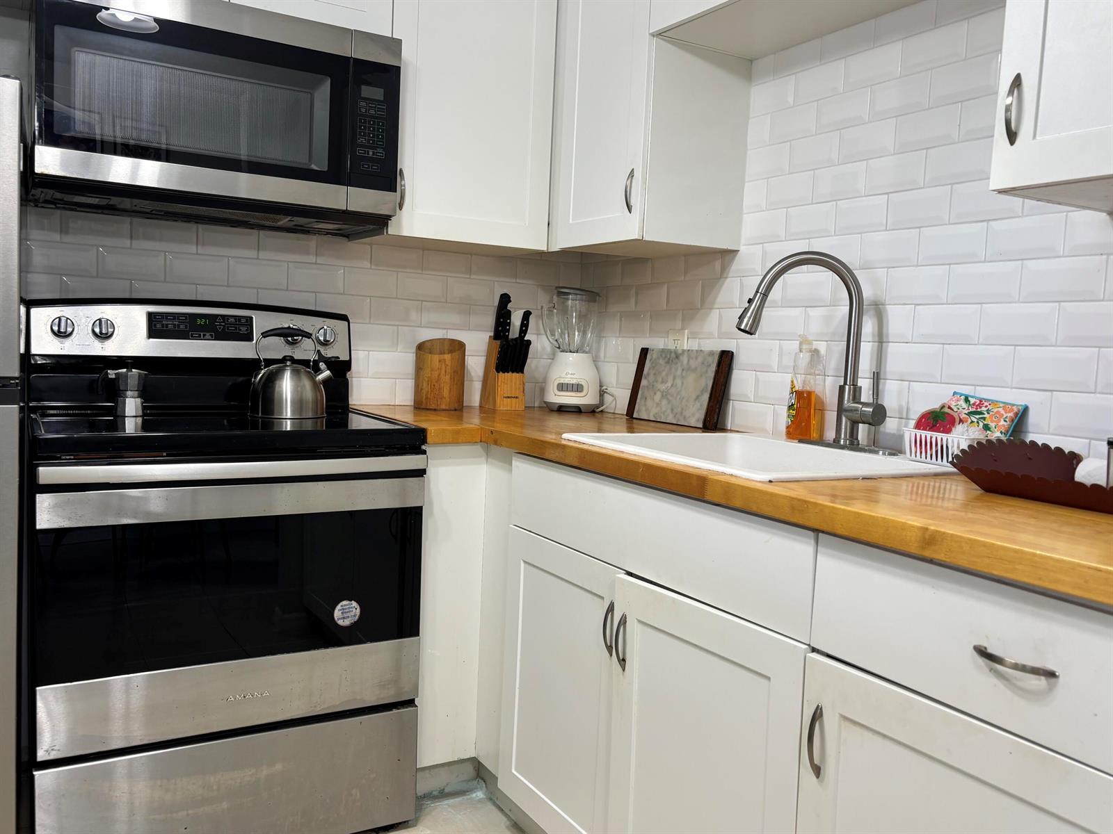 A kitchen features white cabinets, a wood countertop, a white sink, and stainless steel appliances — 243 Northampton M, West Palm Beach FL 33417, WEST PALM BEACH, FL