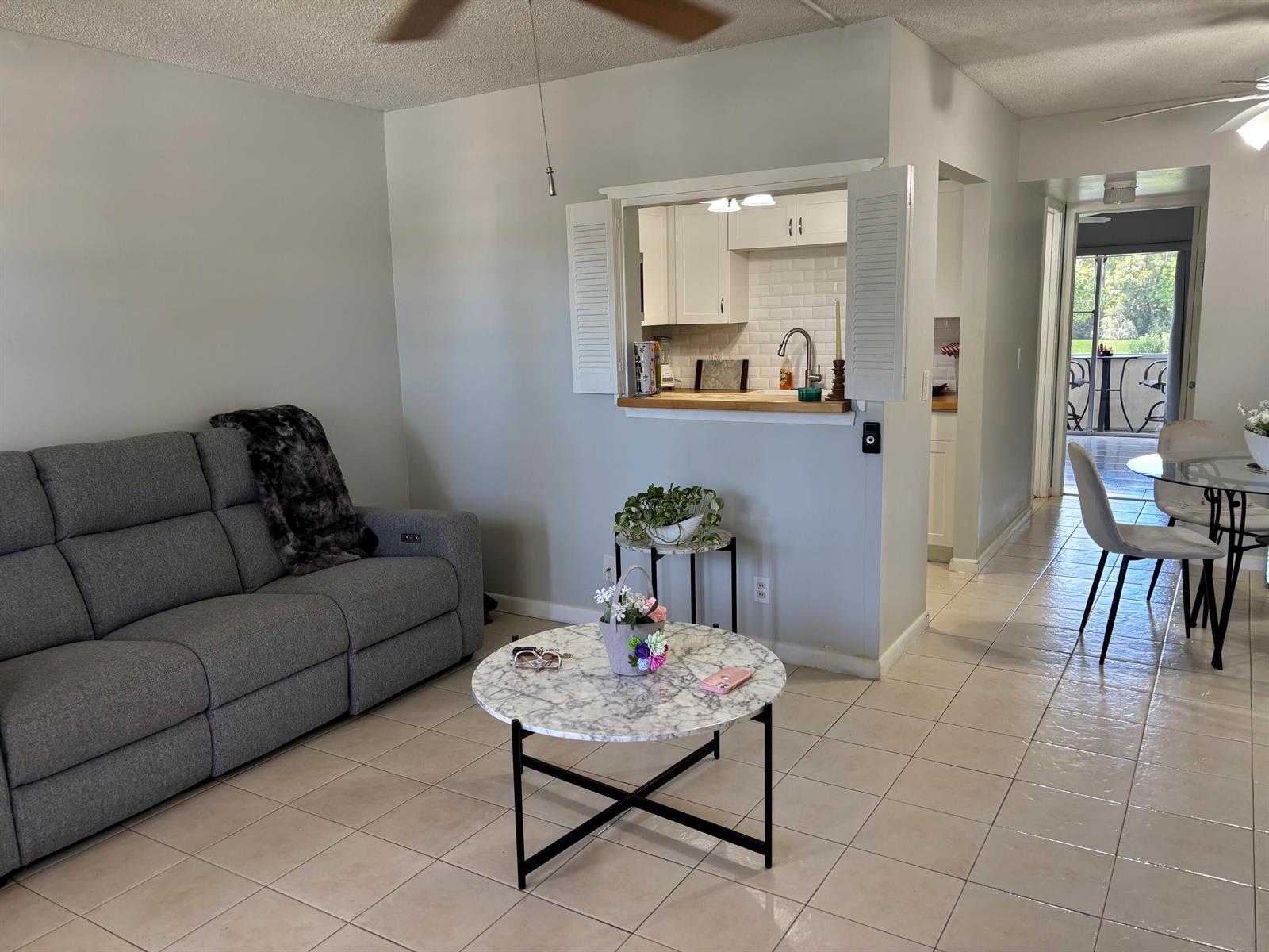 A living room features a gray sofa, marble coffee table, and a kitchen pass-through window — 243 Northampton M, West Palm Beach FL 33417, WEST PALM BEACH, FL