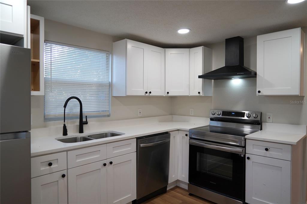 A kitchen features white cabinets, stainless steel appliances, a black range hood, and white countertops — 4509 N 29TH STREET, TAMPA, FL