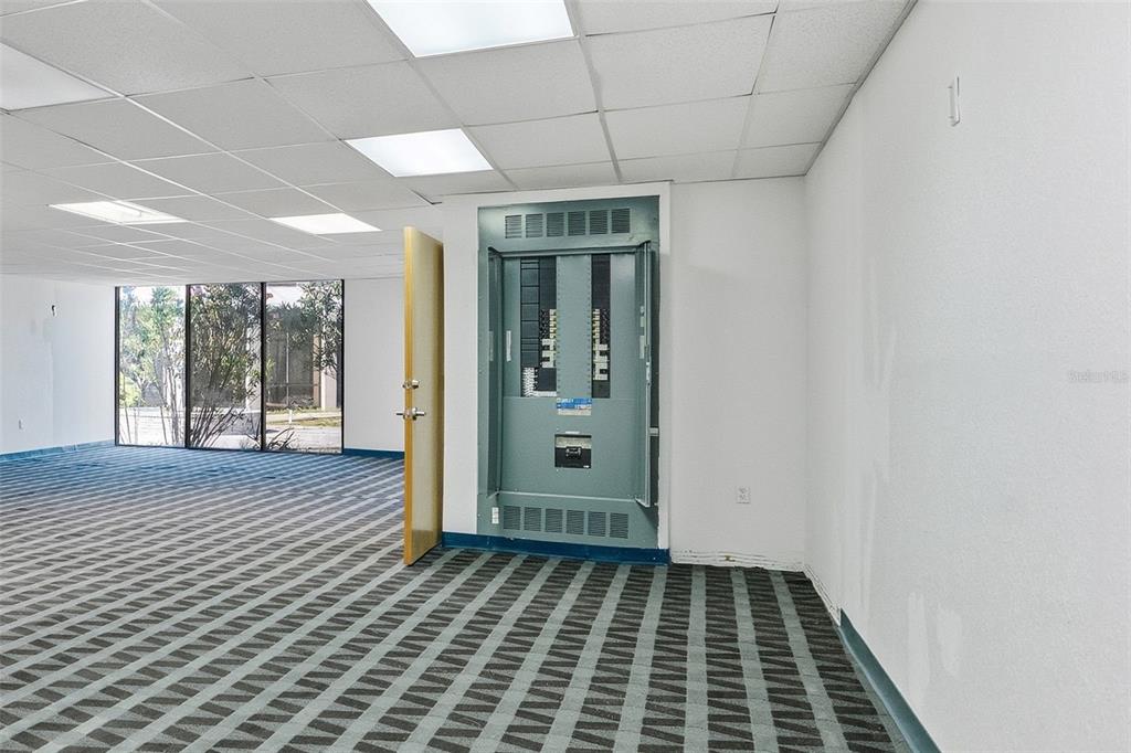 An office room features a large, exposed electrical panel, patterned carpet, and a glass wall — 5341 GRAND BOULEVARD UNIT 103, NEW PORT RICHEY, FL