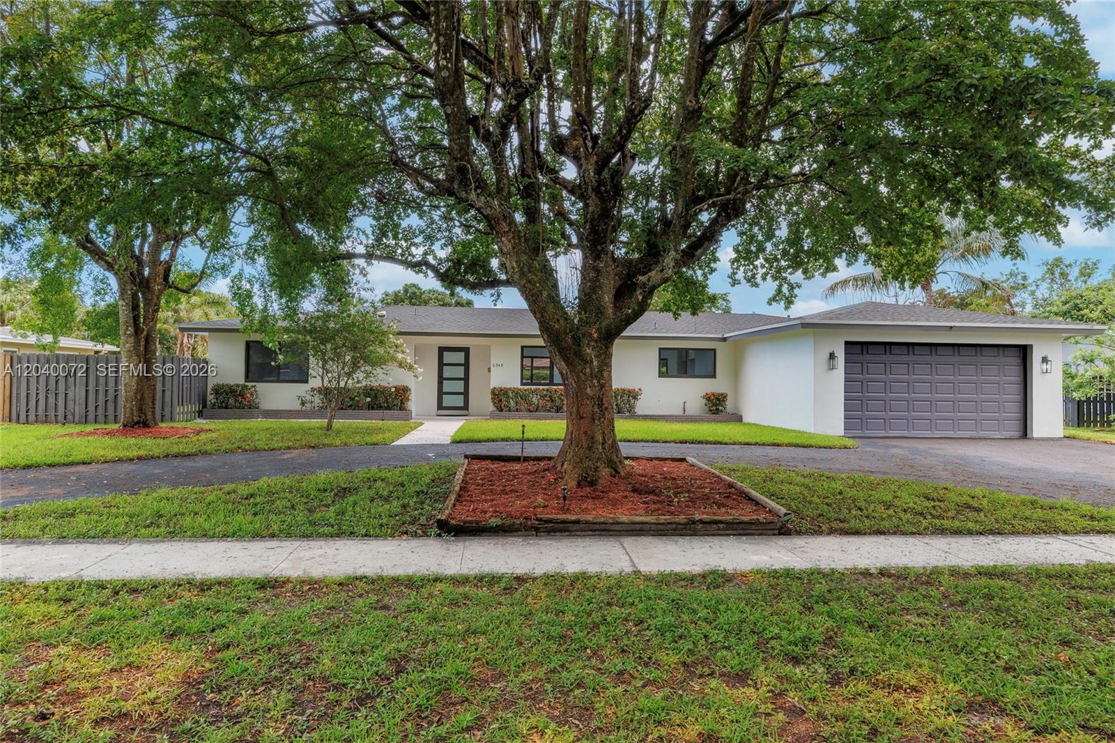 A single-story house with a white exterior, gray garage door, and a large front tree — 6940 NW 6th St, Plantation FL 33317, PLANTATION, FL