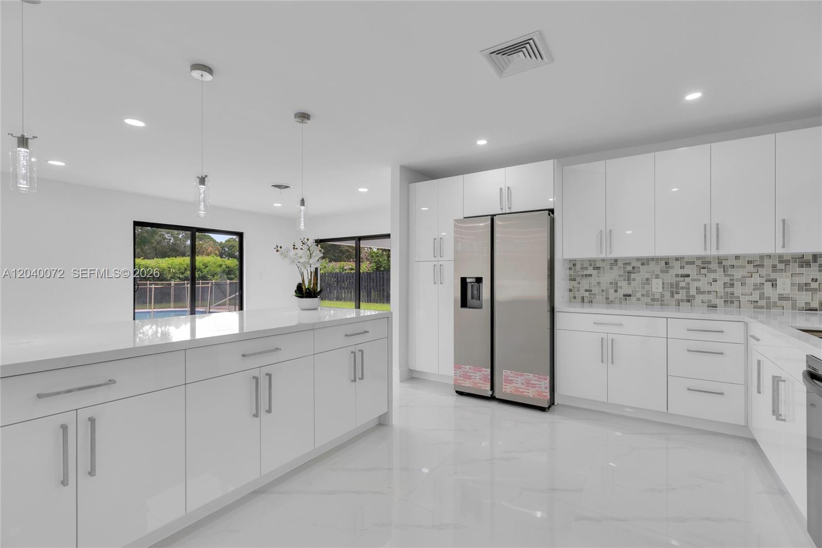 A modern kitchen features white cabinetry, a large island, stainless steel appliances, and tile flooring — 6940 NW 6th St, Plantation FL 33317, PLANTATION, FL