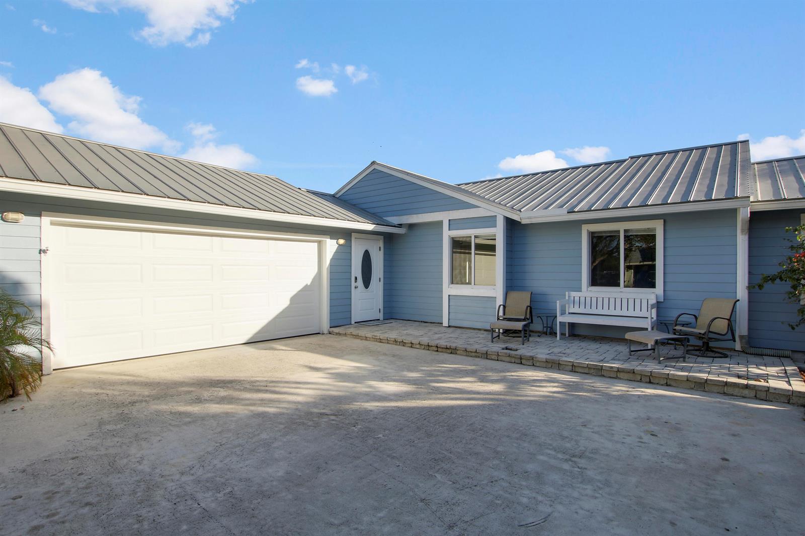 A light blue house with a metal roof, white garage door, and a paved patio — 18162 Jupiter Landings Drive, Jupiter FL 33458, JUPITER, FL
