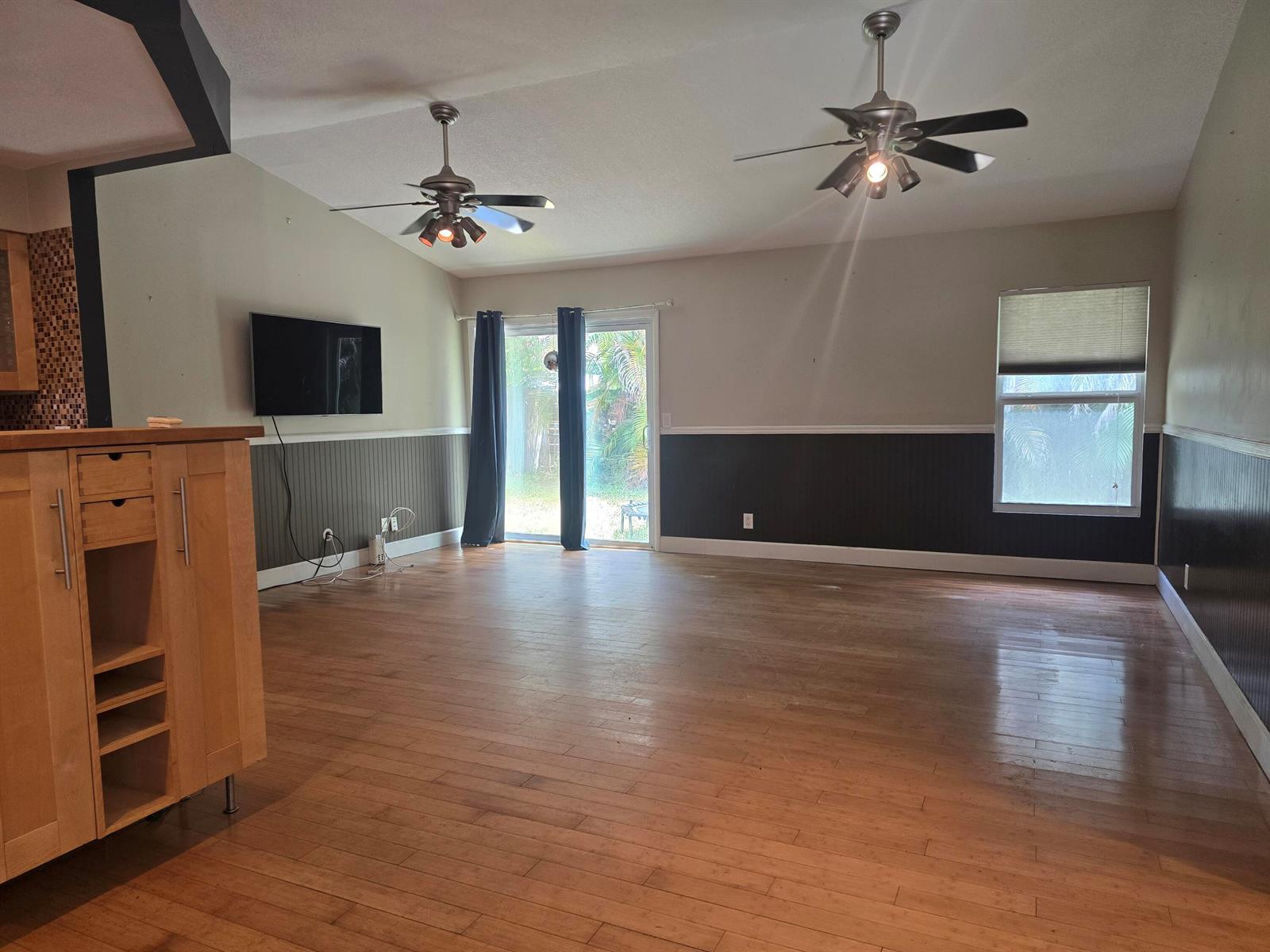 An empty living room features hardwood floors, two ceiling fans, and dark wainscoting on walls — 18162 Jupiter Landings Drive, Jupiter FL 33458, JUPITER, FL