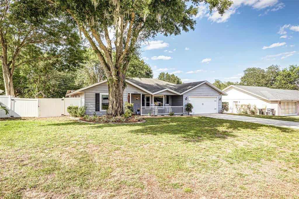 A single-story gray house with a white garage door and a large front yard tree — 2326 ARROWHEAD BOULEVARD, LAKELAND, FL
