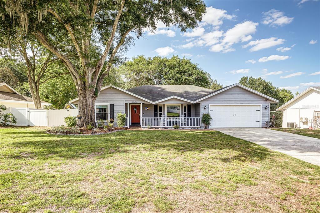 A single-story house with gray siding, a white garage door, and a large front tree — 2326 ARROWHEAD BOULEVARD, LAKELAND, FL