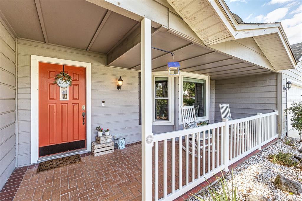 A covered front porch features a red door, brick flooring, and a white railing — 2326 ARROWHEAD BOULEVARD, LAKELAND, FL