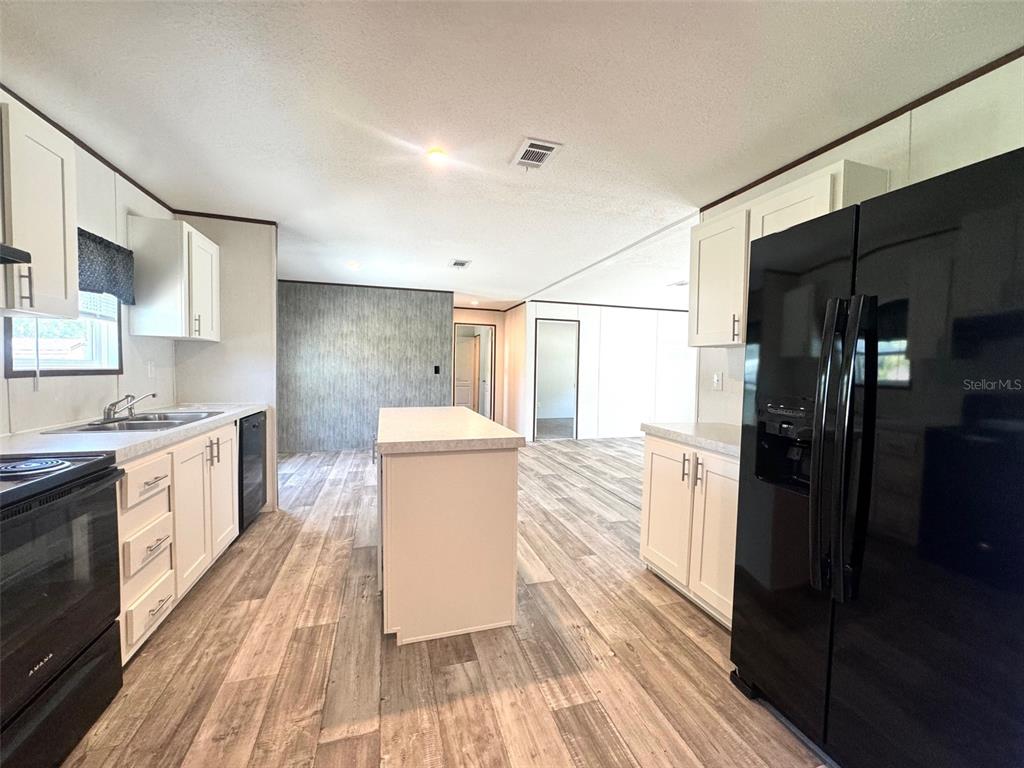 A kitchen features white cabinets, black appliances, a central island, and wood-look flooring — 389 WATERVIEW DRIVE, POLK CITY, FL