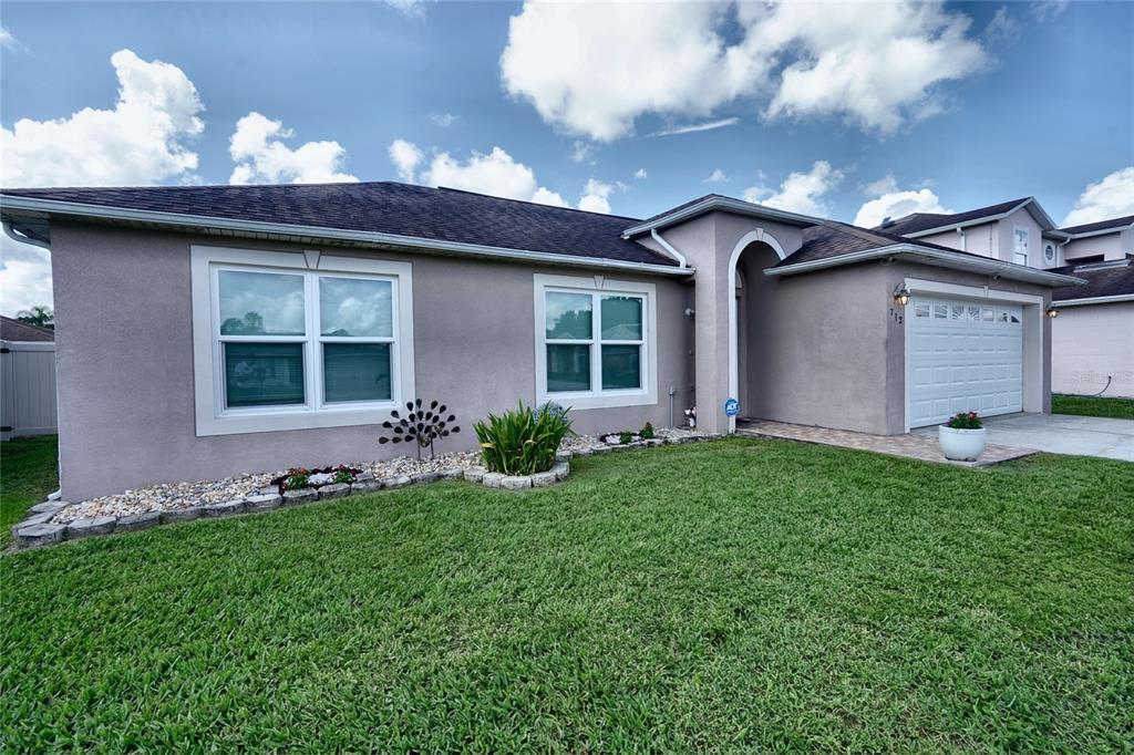 A single-story house with a tan stucco exterior, a two-car garage, and a front lawn — 712 BEAR WAY, POINCIANA, FL