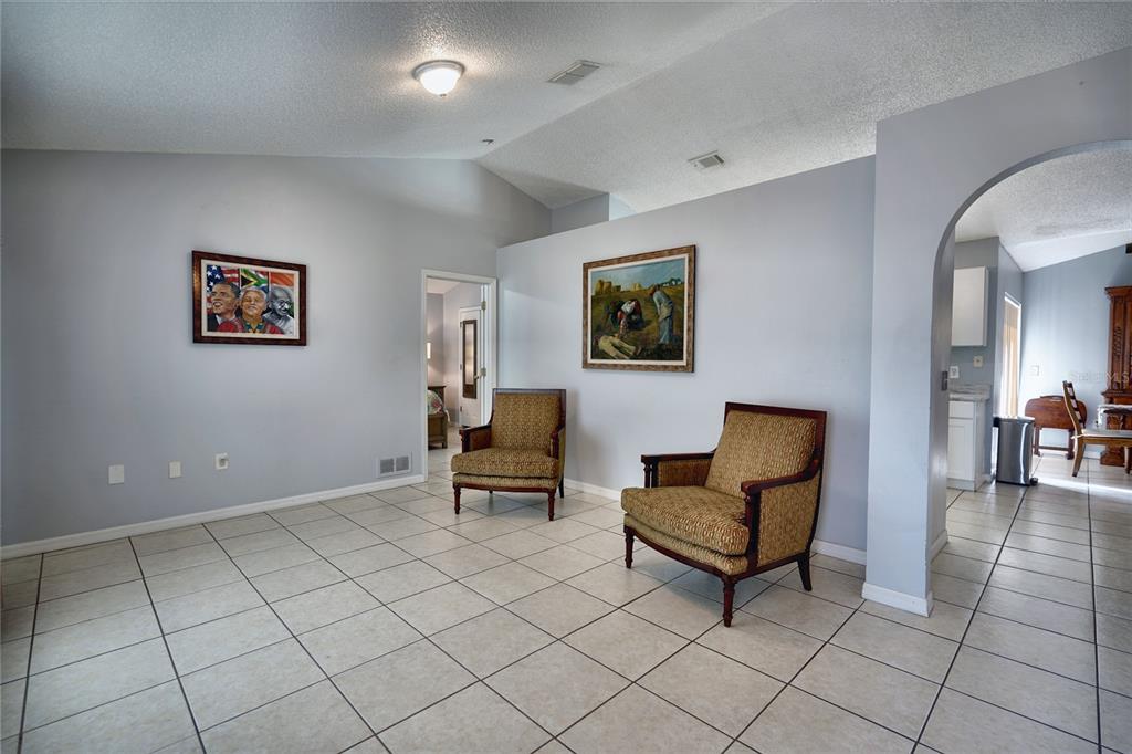 A living area with light gray walls, tiled floors, two patterned armchairs, and framed artwork — 712 BEAR WAY, POINCIANA, FL