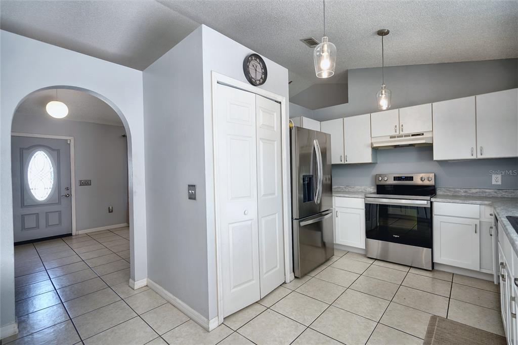 A kitchen with white cabinets, stainless steel appliances, and tile flooring, adjacent to an entryway — 712 BEAR WAY, POINCIANA, FL