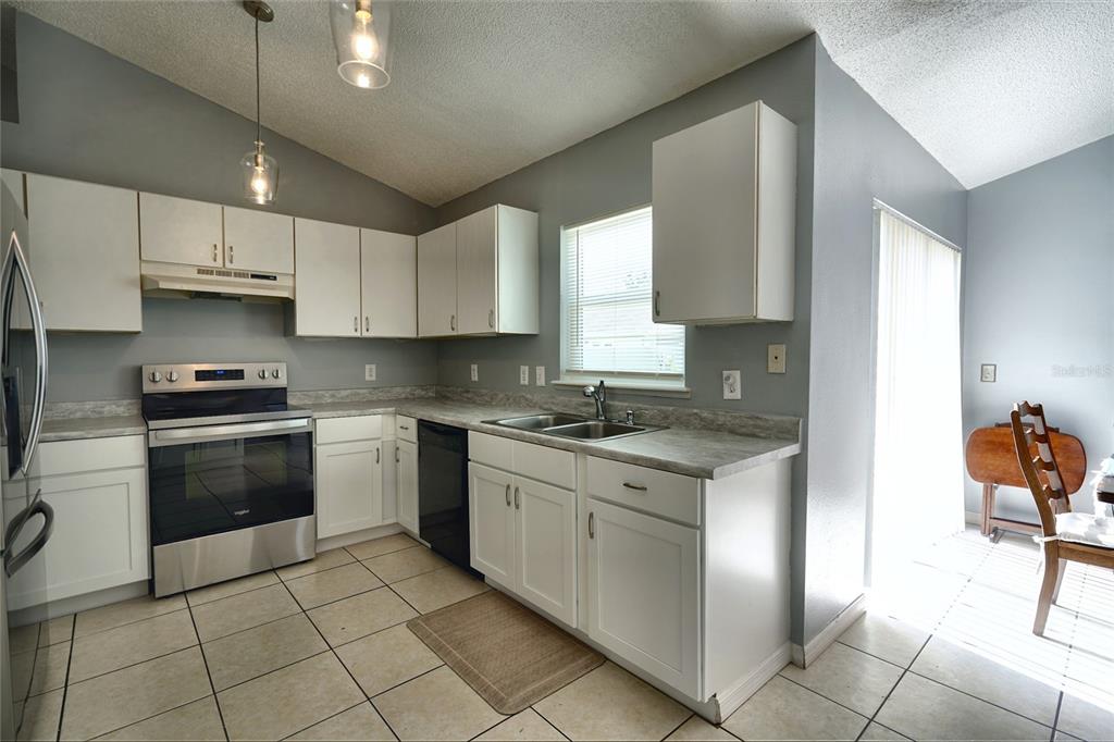 A kitchen features white cabinets, stainless steel appliances, gray countertops, and light-colored tile flooring — 712 BEAR WAY, POINCIANA, FL