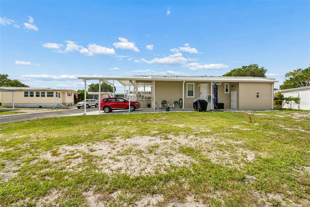 A tan manufactured home with a carport and a red SUV parked underneath — 9790 66TH STREET N UNIT 210, PINELLAS PARK, FL