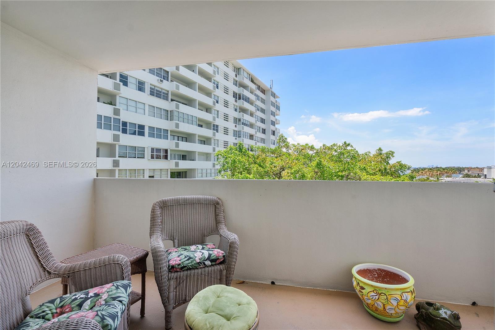 A balcony features wicker chairs, a small table, a green ottoman, and a decorative planter — 5 Island Ave # 6A, Miami Beach FL 33139, MIAMI BEACH, FL