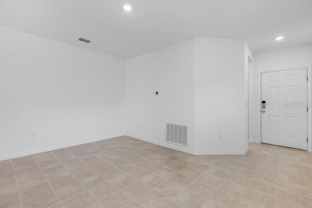 An empty room with white walls, beige tile flooring, and a white front door — 13803 SHELLMORE AVENUE, PALMETTO, FL