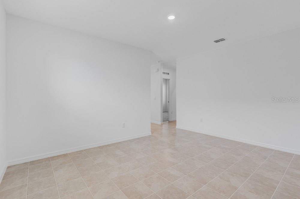 An empty room with white walls and light-colored tile flooring leads to a hallway — 13803 SHELLMORE AVENUE, PALMETTO, FL