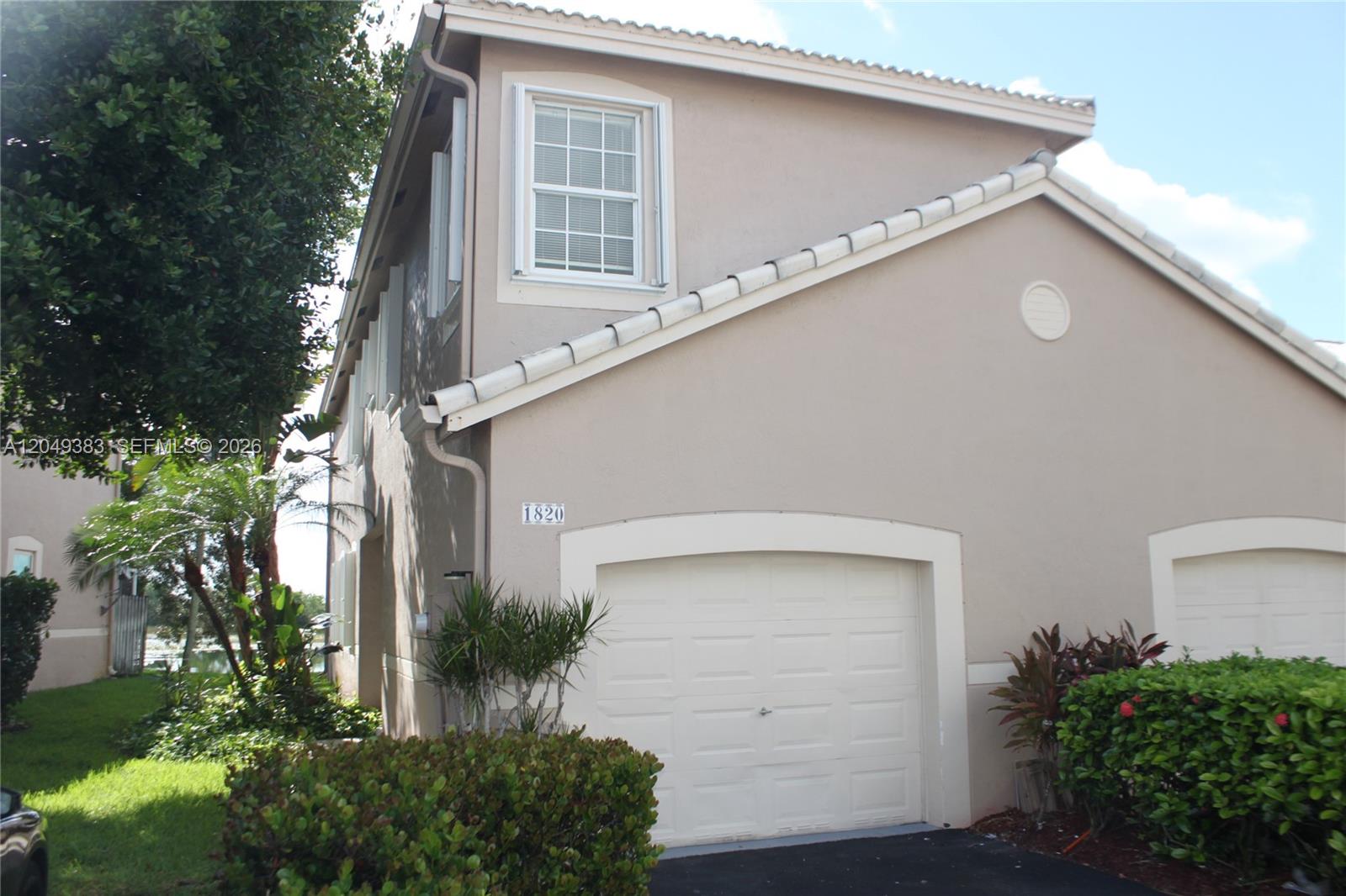 A two-story tan stucco townhouse features a white garage door and a side entryway — 1820 Salerno Cir, Weston FL 33327, WESTON, FL