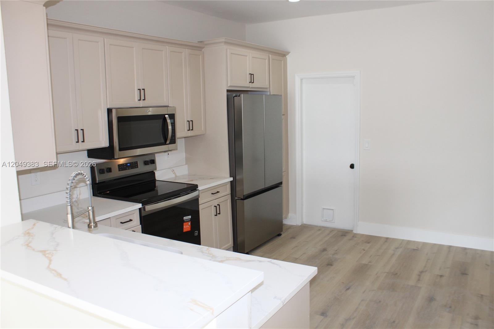 A kitchen features cream-colored cabinets, stainless steel appliances, and white countertops with gold veining — 1820 Salerno Cir, Weston FL 33327, WESTON, FL