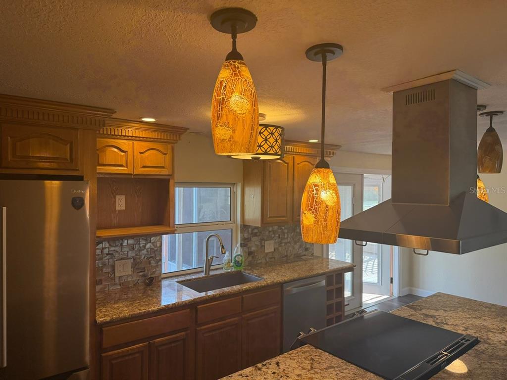 A kitchen features wood cabinets, granite countertops, stainless steel appliances, and three hanging pendant lights — 11595 SE 129TH PLACE, OCKLAWAHA, FL