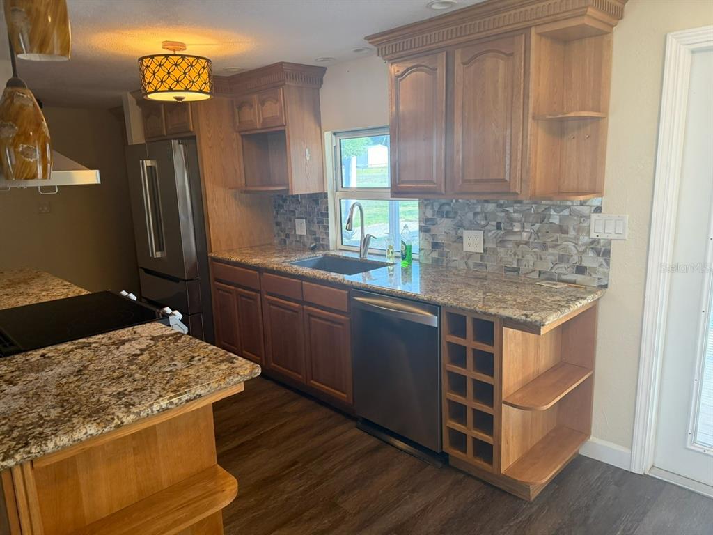 A kitchen features wood cabinets, granite countertops, a stainless steel dishwasher, and a wine rack — 11595 SE 129TH PLACE, OCKLAWAHA, FL