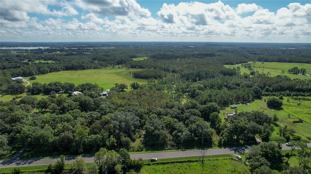 An aerial view shows a rural landscape with a road, dense trees, and open fields — 5804 STATE ROAD 33, CLERMONT, FL