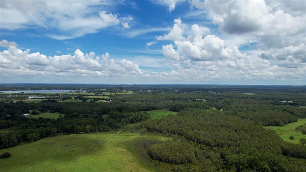 An aerial view shows a large expanse of green fields, dense forests, and a distant lake — 5804 STATE ROAD 33, CLERMONT, FL