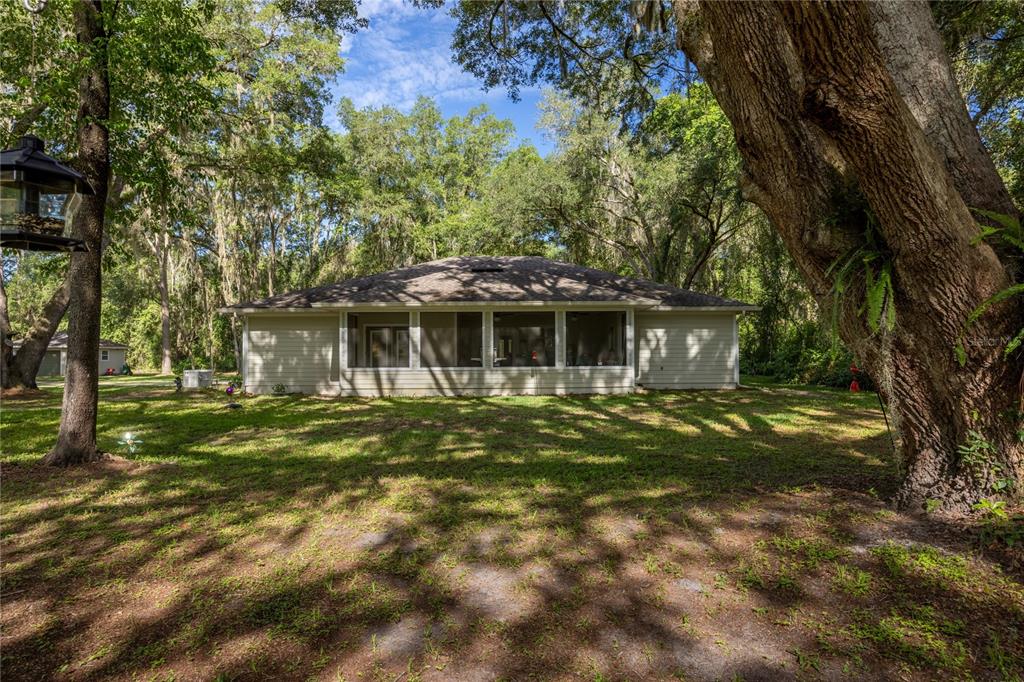 The rear exterior of a single-story house features a screened-in porch surrounded by large trees — 7517 NE 221ST STREET, MELROSE, FL