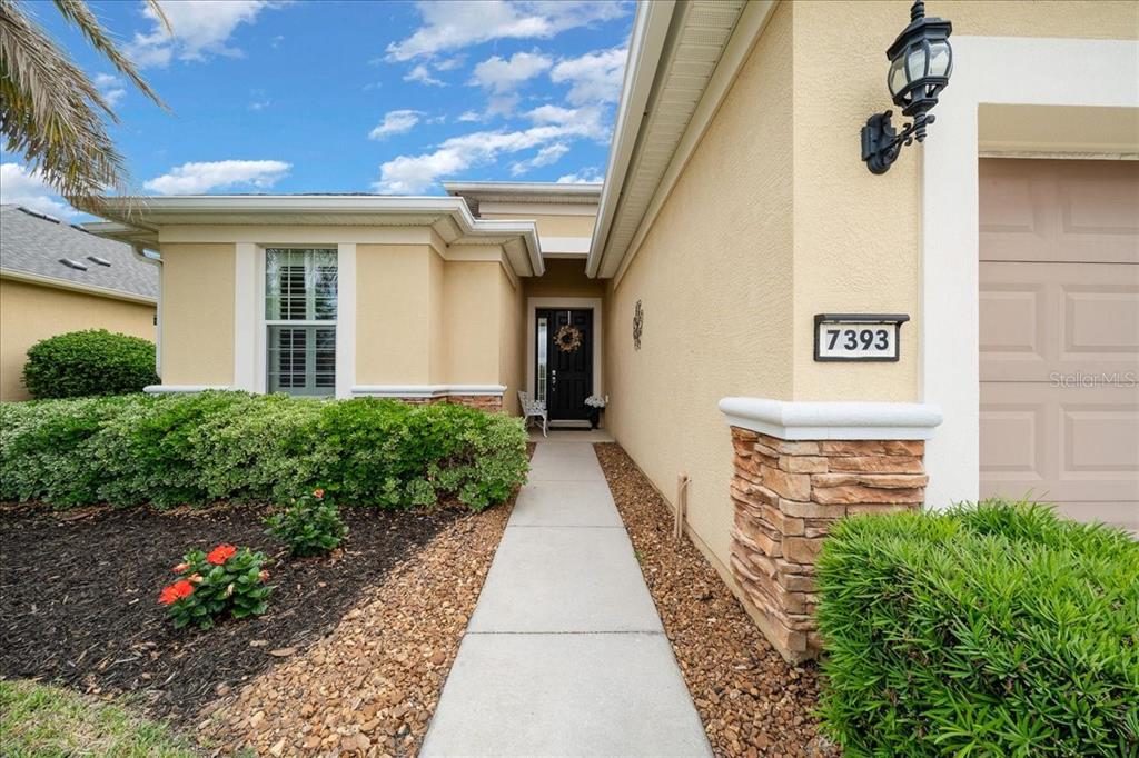 The exterior of a house features a tan stucco facade, stone accents, and a walkway — 7393 SW 100TH COURT, OCALA, FL