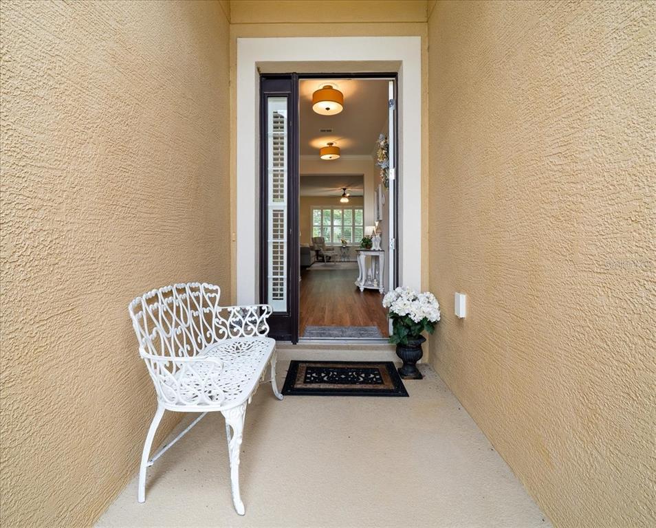 A white metal bench sits on a covered porch outside an open front door — 7393 SW 100TH COURT, OCALA, FL