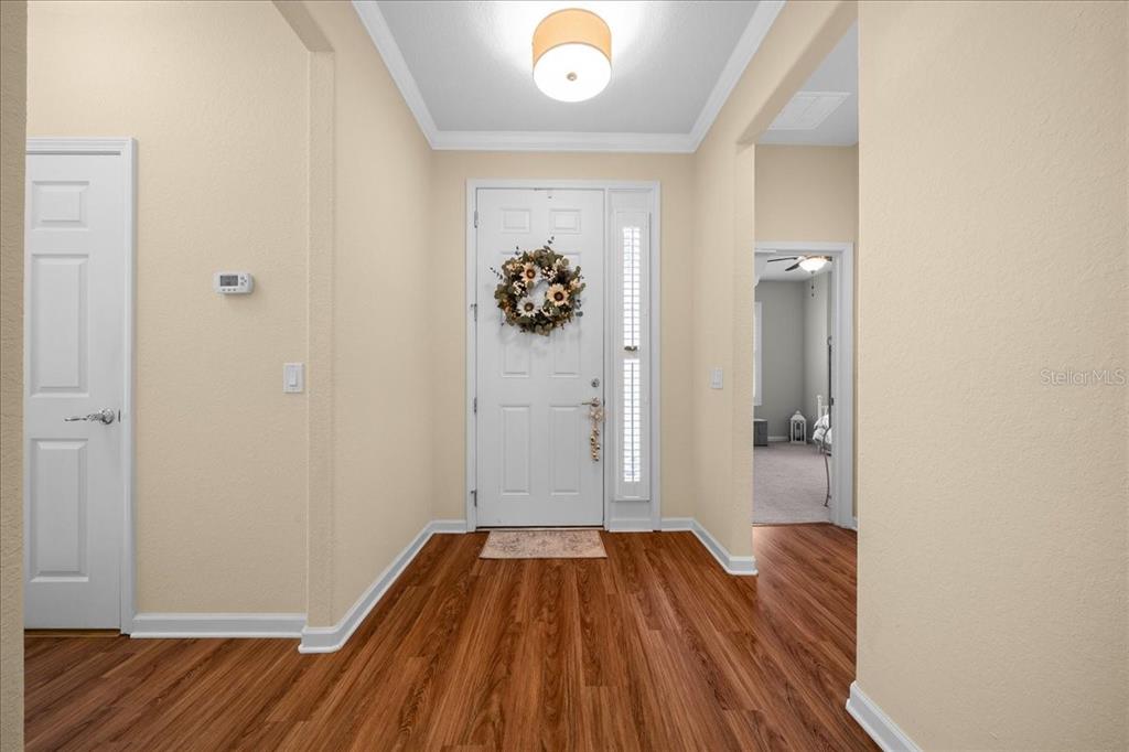 An entryway with wood-look flooring, a white front door with a wreath, and beige walls — 7393 SW 100TH COURT, OCALA, FL