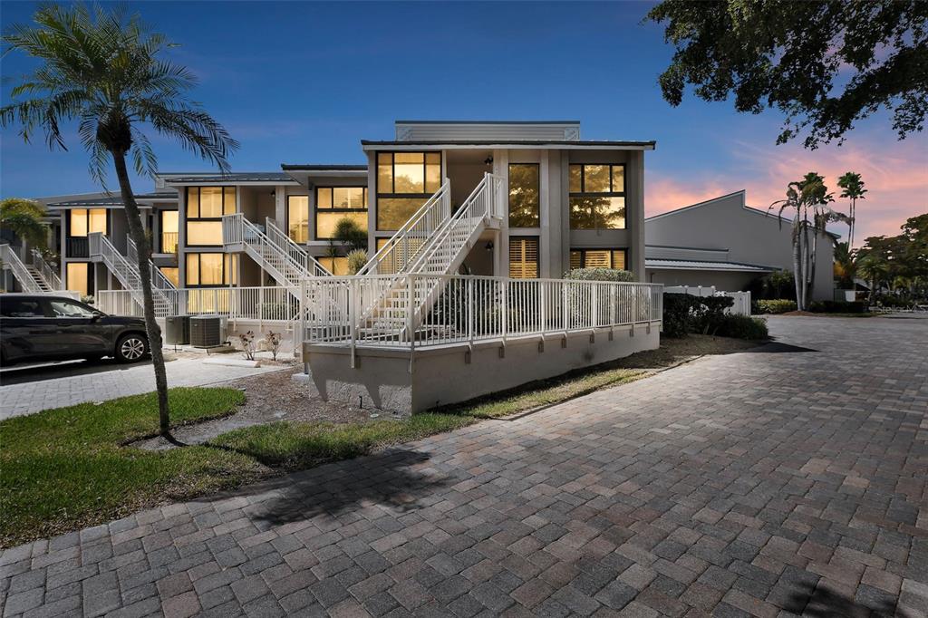 A multi-story apartment building with exterior staircases and a paved driveway at dusk — 5655 GULF OF MEXICO DRIVE UNIT D107, LONGBOAT KEY, FL
