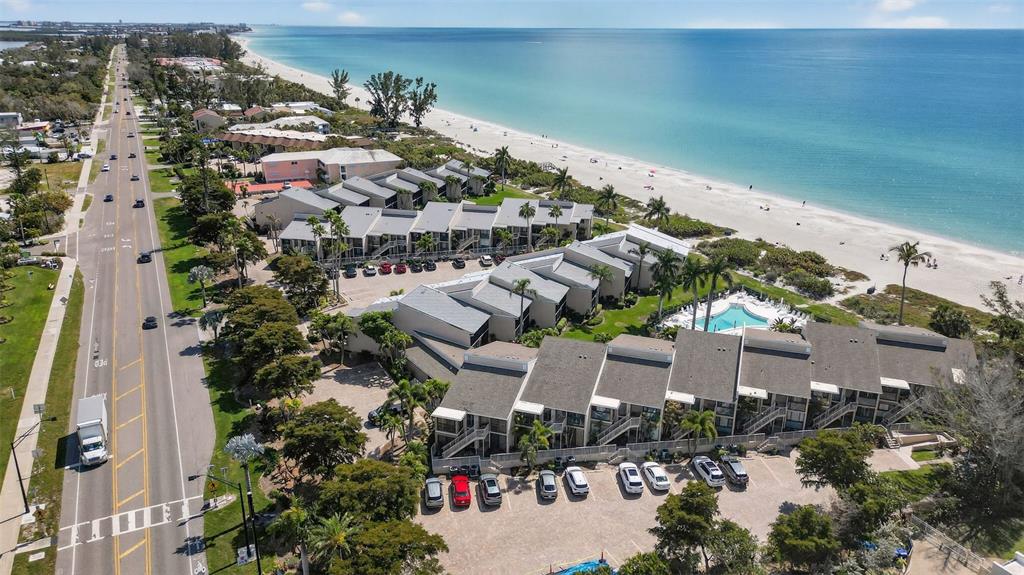 An aerial view shows a beachfront condominium complex with a swimming pool and parking lot — 5655 GULF OF MEXICO DRIVE UNIT D107, LONGBOAT KEY, FL