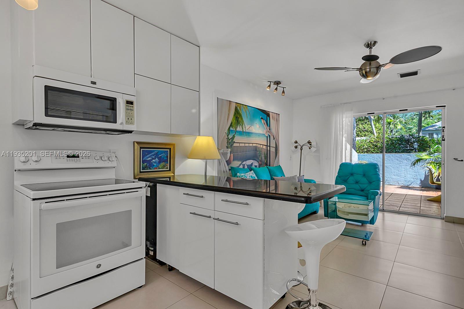 A kitchen with white cabinets and appliances opens into a living area with a patio — 798 Crandon Blvd # C, Key Biscayne FL 33149, KEY BISCAYNE, FL