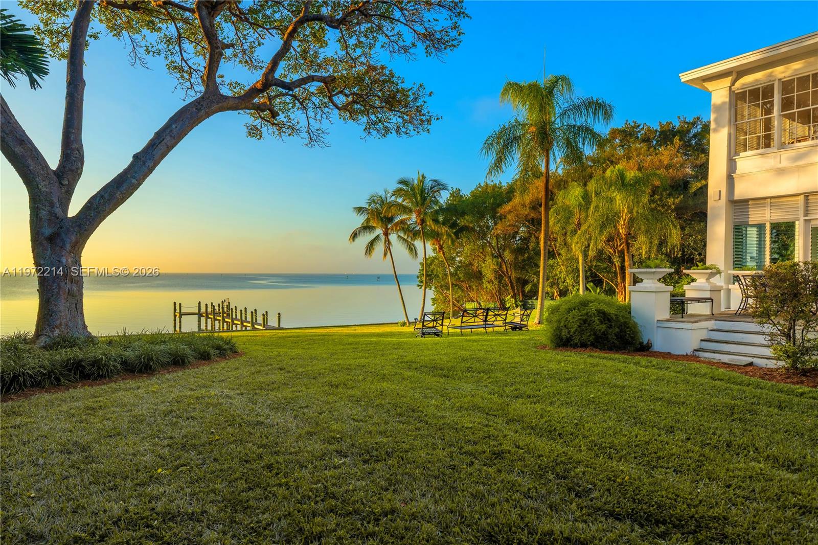 A grassy lawn leads to a waterfront view with palm trees and a house exterior — 3149 Brickell Ave, Miami FL 33129, MIAMI, FL