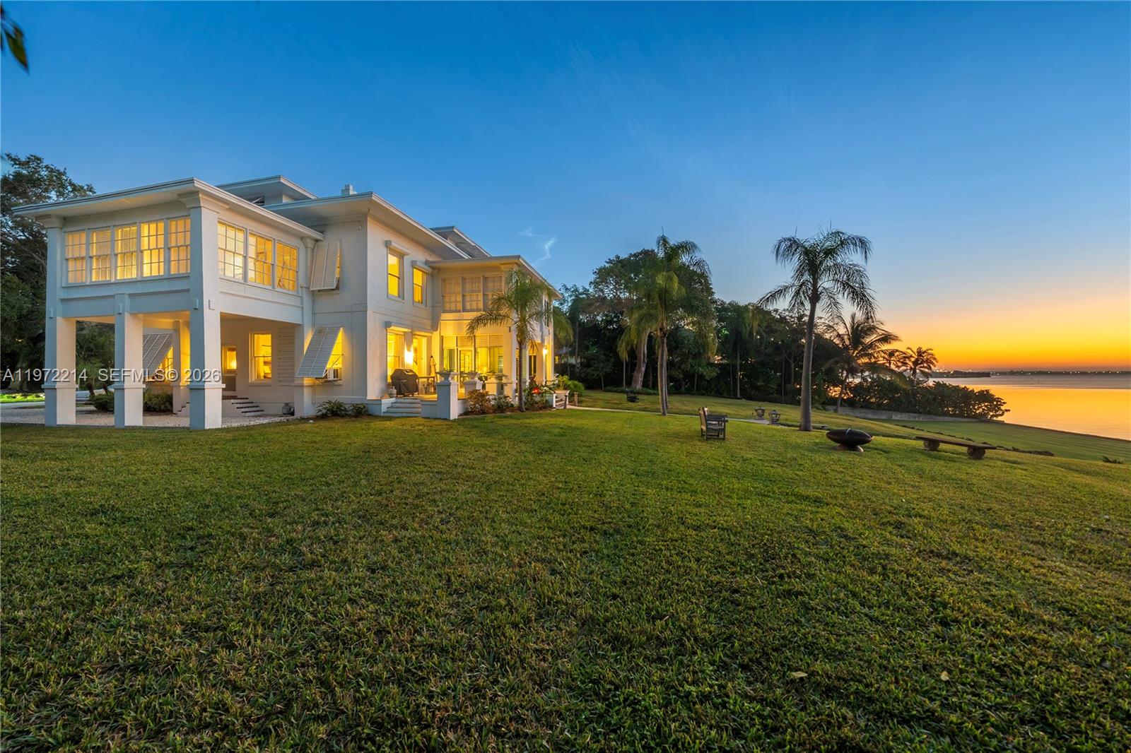 A large white two-story house sits on a grassy lawn overlooking a sunset waterfront — 3149 Brickell Ave, Miami FL 33129, MIAMI, FL